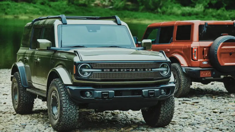 Two 2027 Ford Bronco Filson SUVs, one green and one copper First Edition, parked on gravel