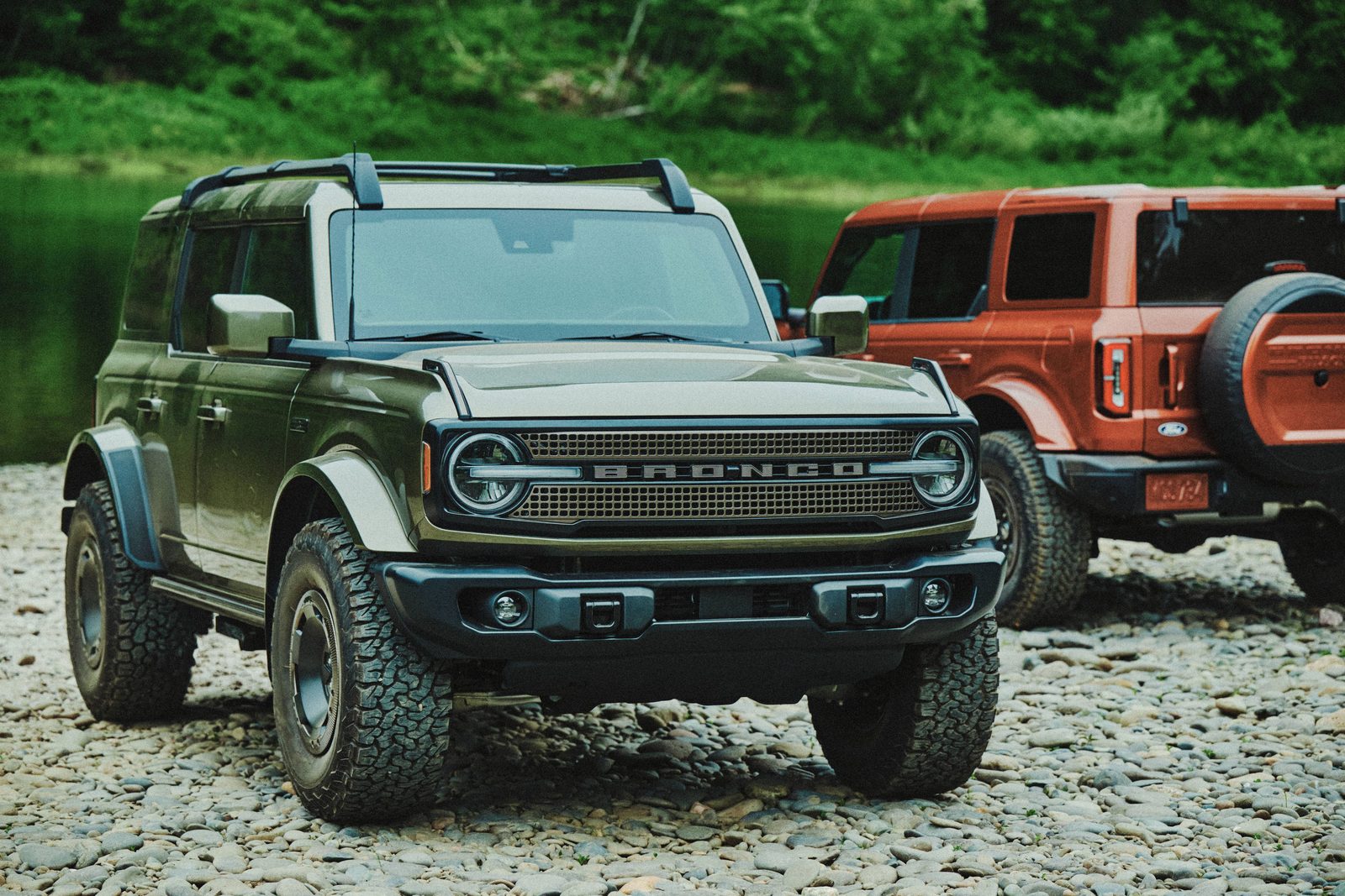 Two 2027 Ford Bronco Filson SUVs, one green and one copper First Edition, parked on gravel