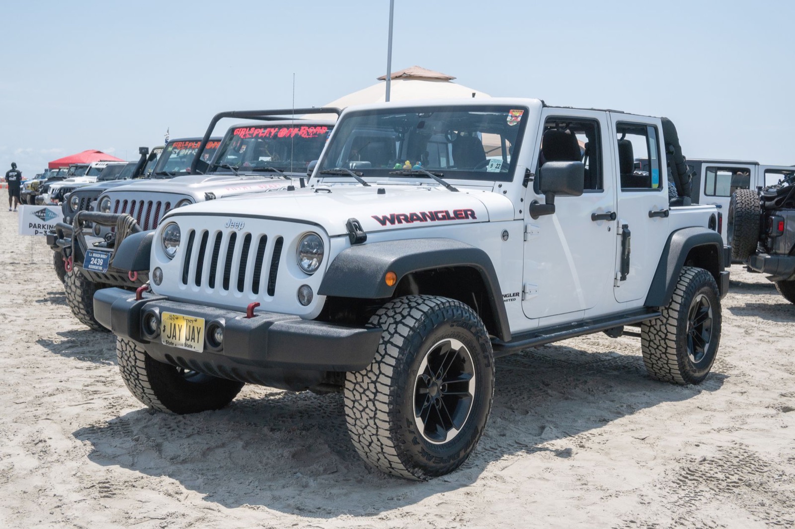 White Jeep Wrangler Unlimited of the previous JK generation parked on sand among other Jeeps