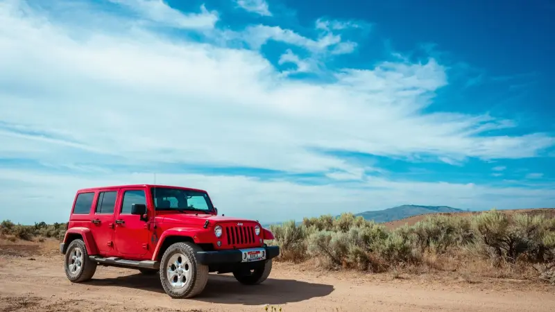 Red Jeep Wrangler Unlimited of the previous JK generation parked on a dirt road under a blue sky