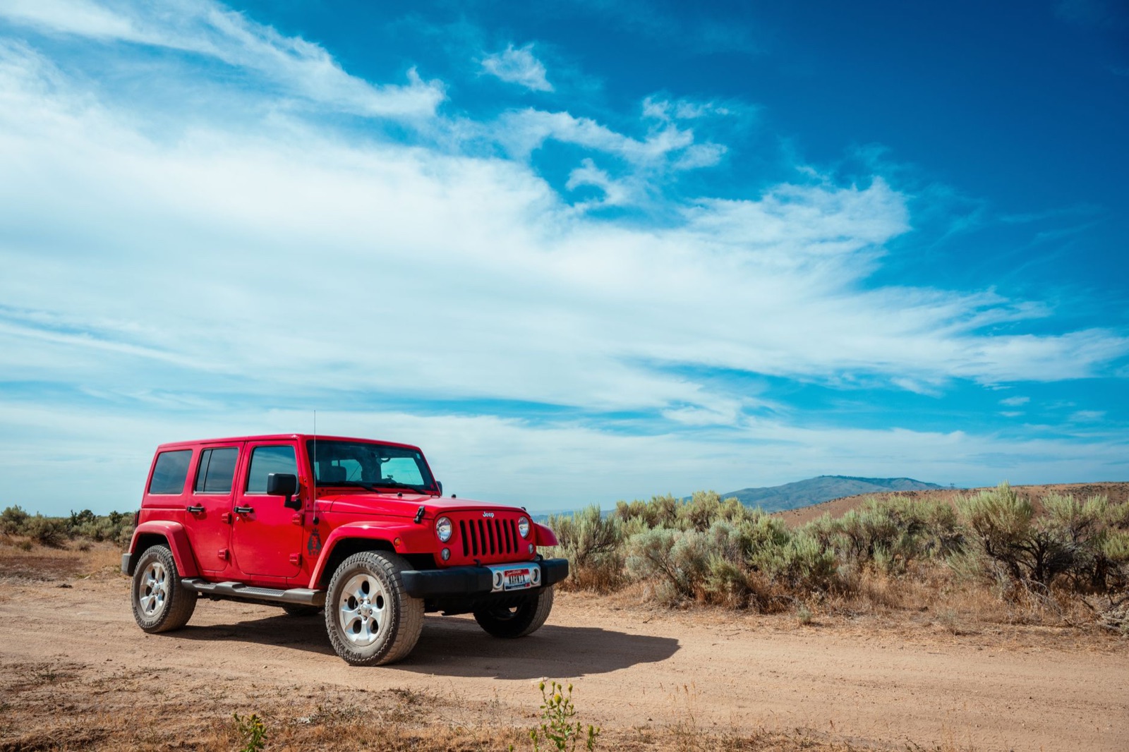 Red Jeep Wrangler Unlimited of the previous JK generation parked on a dirt road under a blue sky